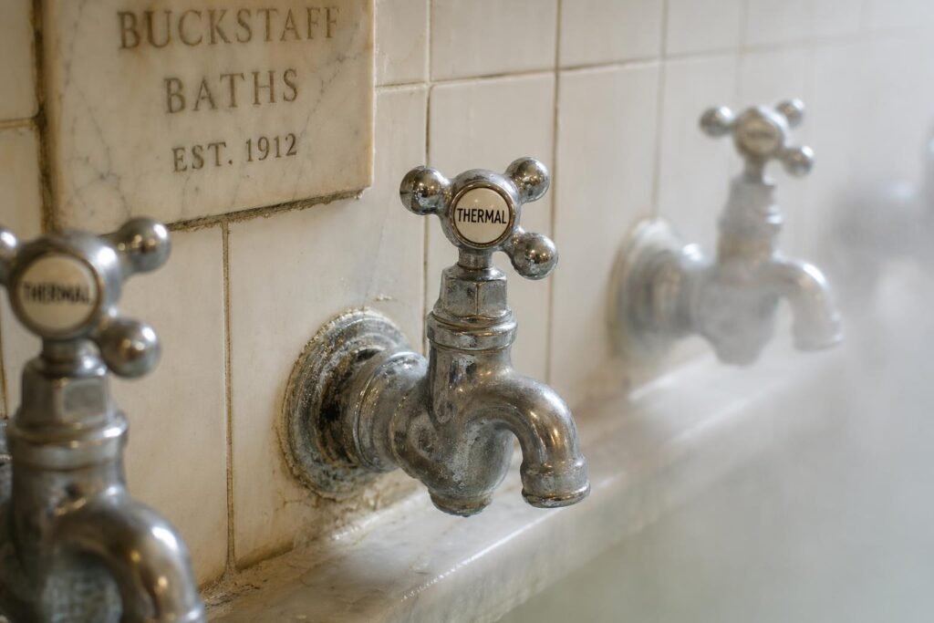 Chrome thermal water taps against white tile, slight mineral deposits visible, steam rising softly from an unseen bath just out of frame.