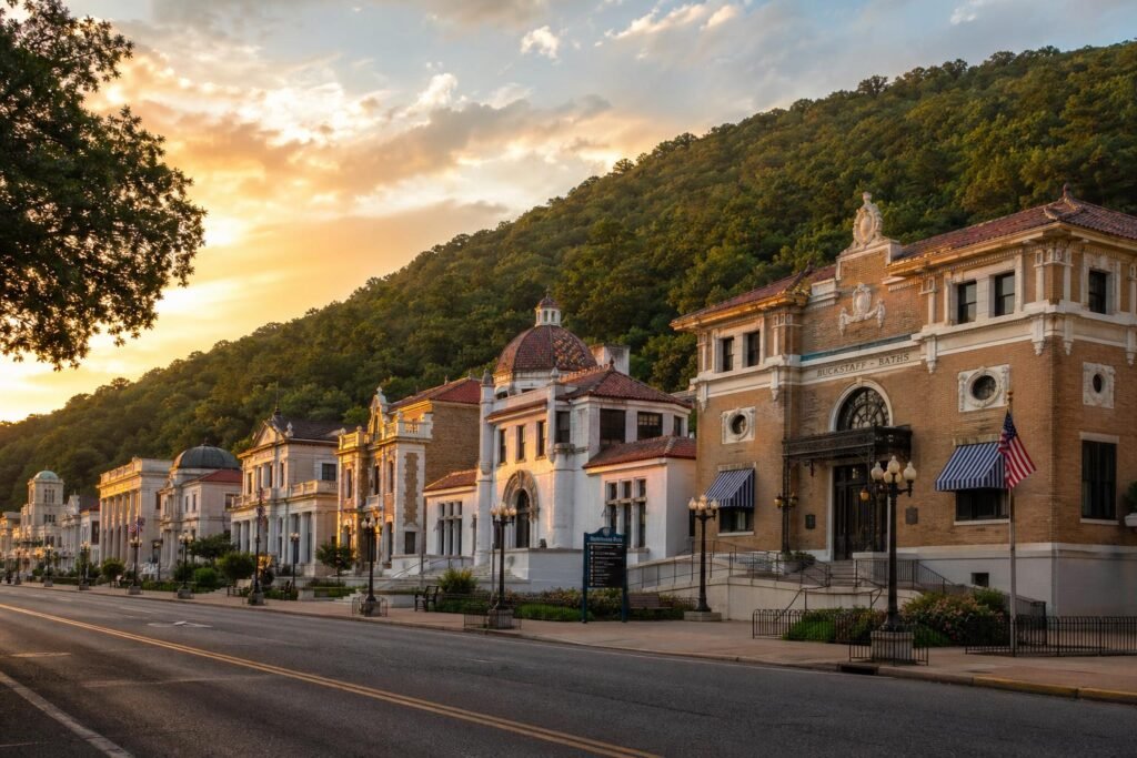 Eight historic limestone and brick bathhouses lined up like beaux-arts dominoes along Central Avenue, with the forested mountain rising behind them
