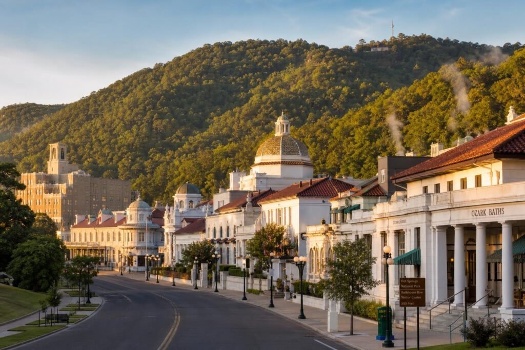 Bathhouse Row's terra cotta roofs and white columns line Central Avenue with wooded mountains rising behind, steam wisps barely visible from morning vents
